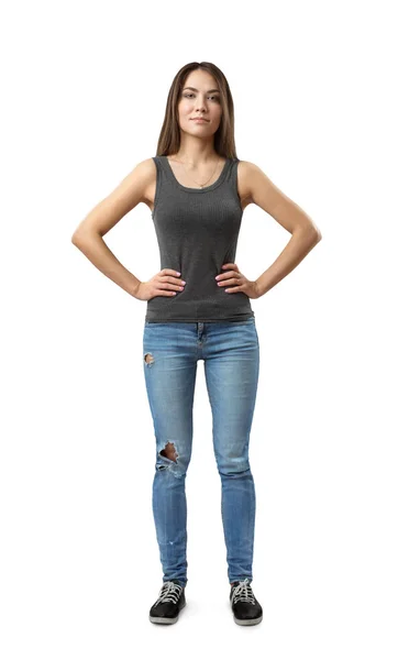 Vorderseite der jungen attraktiven Frau in grauem ärmellosen Oberteil und blauen Jeans, die mit Armen auf Taille isoliert auf weißem Hintergrund steht. — Stockfoto