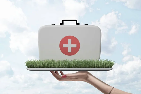 Visão lateral de mulheres mão segurando bandeja com patch de grama verde nele com médicos caso em cima contra o céu nublado . — Fotografia de Stock