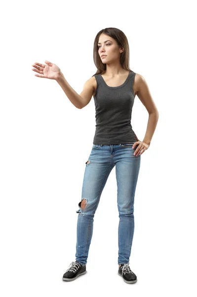 Молода жінка у сірому верхньому та синьому джинсах стоїть, одна рука на стегні та інша рука тримається, як ніби на невидимому екрані, ізольована на білому тлі . — стокове фото