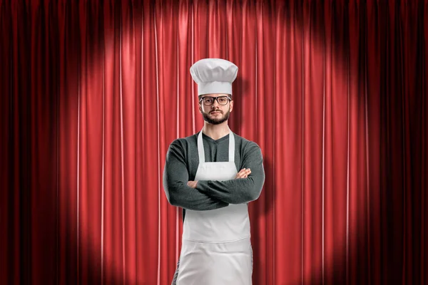 Koch trägt Küchenschürze und Kochmütze auf rotem Bühnenvorhang Hintergrund — Stockfoto