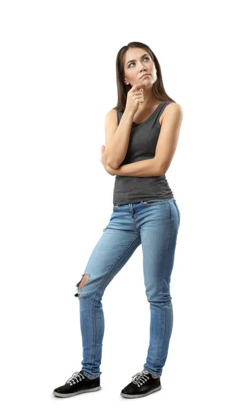 Kvinna i grå topp och blå jeans står med tankeväckande uttryck i ansiktet och med handen på hakan tittar upp isolerad på vit bakgrund. — Stockfoto