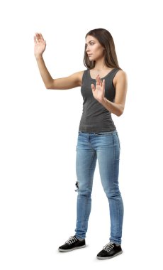 Gri üst ve mavi kot pantolon içinde fit güzel kadın beyaz arka plan üzerinde izole görünmez ekran dokunmadan sanki elleri yükseltilmiş ile yarım dönüş poz ayakta.