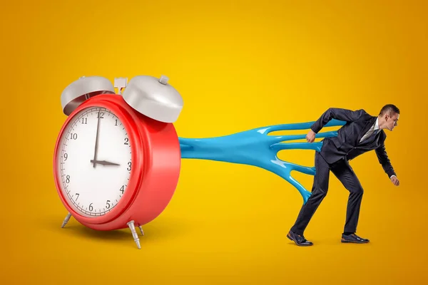 Young businessman stuck to red alarm clock with blue sticky slime on yellow background — Stock Photo, Image