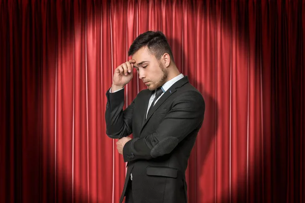 Young businessman thinking on red stage curtains background