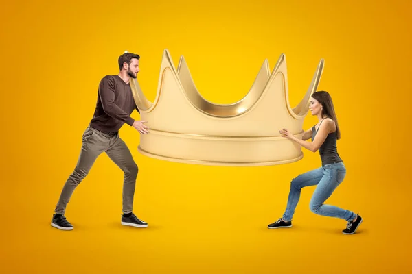 Vista lateral del hombre y la mujer, ambos en ropa casual, llevando una enorme corona de oro sobre fondo amarillo . — Foto de Stock