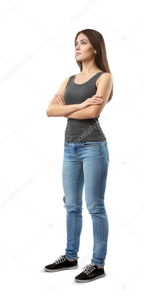 Young woman in gray top and blue jeans standing in half-turn with arms folded, looking up and away, isolated on white background.