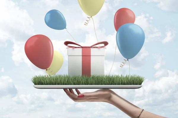 화면에 녹색 잔디와 디지털 태블릿을 들고 여자 손의 측면보기, 상단에 서 선물 상자와 주위에 비행 다채로운 풍선. — 스톡 사진