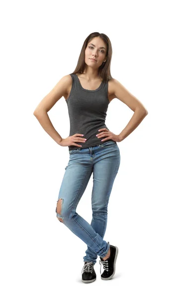 Молода жінка в сірих без рукавів зверху і синіх джинсах стоїть з руками на стегнах і одна нога перед іншою ізольована на білому тлі . — стокове фото