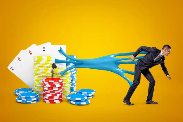 Young businessman stuck to playing cards and casino chips with blue sticky slime on yellow background