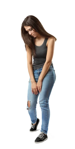 Young sad woman in sleeveless gray top and light-blue jeans standing and looking down isolated on white background. — 스톡 사진