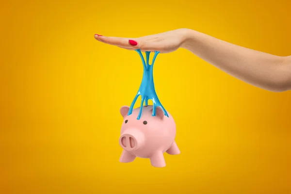 Piggy bank rosa preso à mão feminina com lodo pegajoso azul no fundo amarelo — Fotografia de Stock