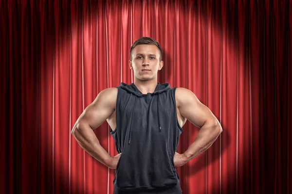 Young muscular man in black sport clothes on red stage curtains background