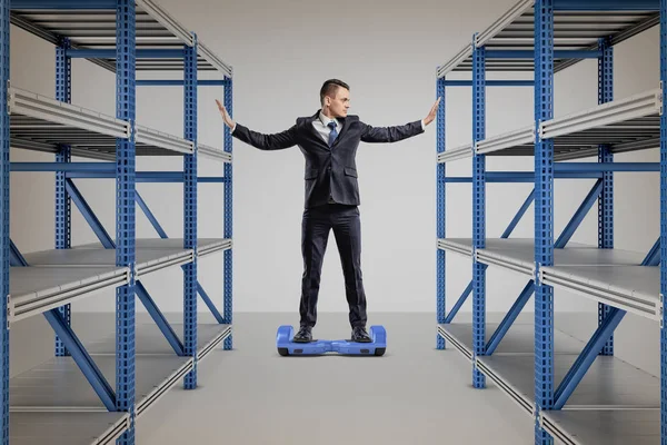 A businessman stands on a self-balancing scooter between two storage racks.