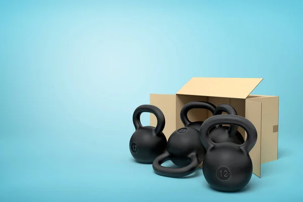 3d rendering of several black kettlebells near open cardboard box that is lying sidelong on light-blue background with copy space.