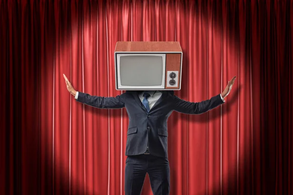 Empresario con televisor vintage en lugar de la cabeza levantando los brazos sobre fondo de cortinas de escenario rojo — Foto de Stock