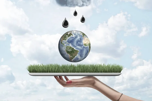 Closeup of womans hand holding digital tablet with grass on screen, little Earth in air above it and black drops falling from grey cloud above.