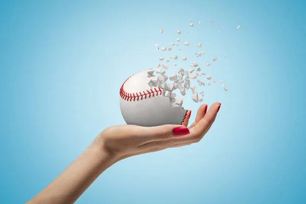 Tangan wanita memegang bola bisbol kecil hancur berkeping-keping di latar belakang biru — Stok Foto