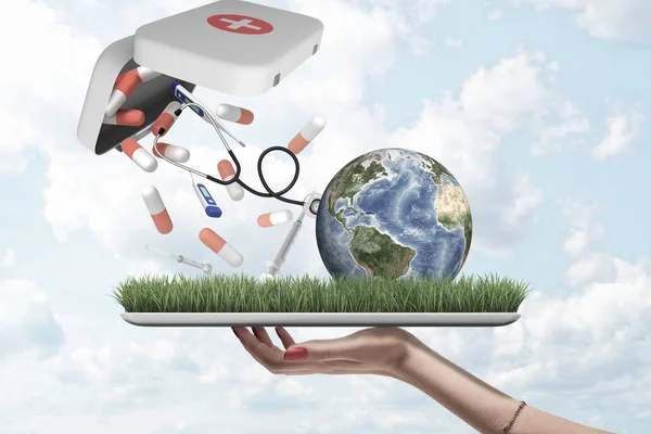 Female hand holding earth globe with pills, syringes and digital thermometers falling out of first aid medical kit on green grass model with blue sky background