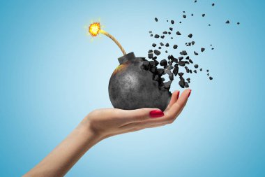 Mavi arka planda parçalara ayrılmış siyah yanan bomba tutan kadın el