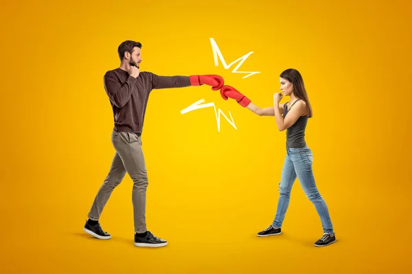 Jeune homme et femme portant des vêtements décontractés et des gants de boxe se battant sur fond jaune — Photo