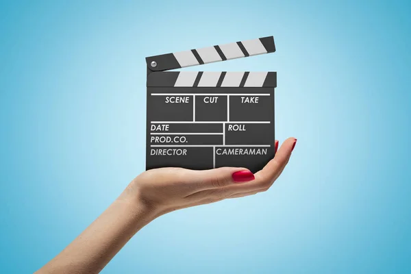 Side closeup of womans hand facing up and holding clapperboard on light-blue gradient background. — Stock Photo, Image