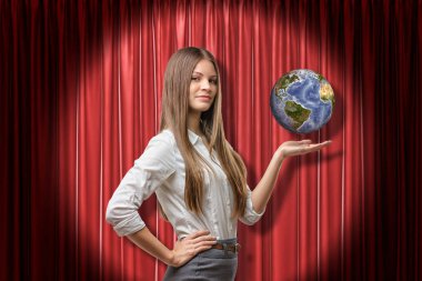 Genç iş kadını kırmızı perde de kalça eliyle yarım dönüş ayakta spot ışık ve yükseltilmiş palmiye üzerinde küçük gezegen Dünya'yı havaya kaldırdı.