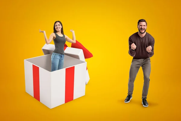 Feliz hombre ganador en ropa casual y chica con jeans y camiseta casual dentro de una caja de regalo grande sobre fondo amarillo — Foto de Stock