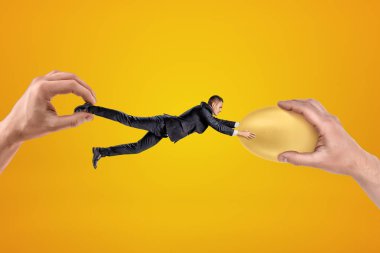 Küçük işadamı iki büyük eliyle zıt yönlere çekiliyor ve iki eliyle de altın yumurtaya tutunuyor..