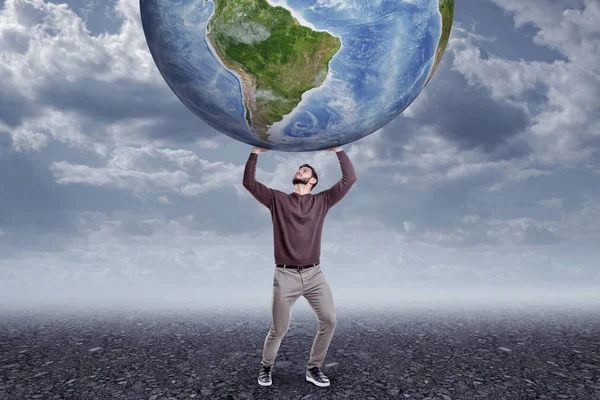 Vista frontal de cuerpo entero del joven con ropa casual sosteniendo el gran globo terráqueo en un día sombrío y nublado . —  Fotos de Stock