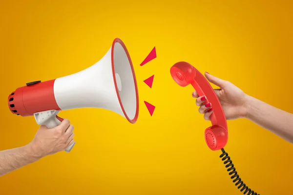 Red and white megaphone in mans hand on the left is speaking right into red retro phone receiver in womans hand on the right.