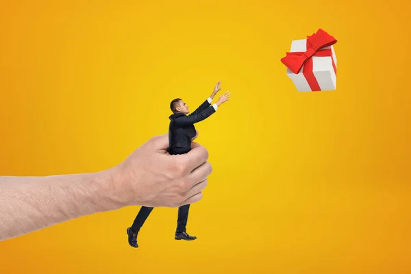 Grote mannelijke hand holding zakenman reiken naar geschenk doos op gele achtergrond — Stockfoto
