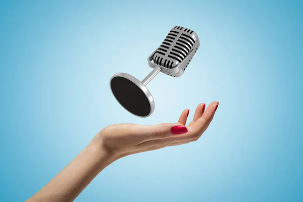 Seitliche Nahaufnahme der nach oben gerichteten Frauenhand und des schwebenden Mikrofons auf hellblauem Gradienten-Hintergrund. — Stockfoto