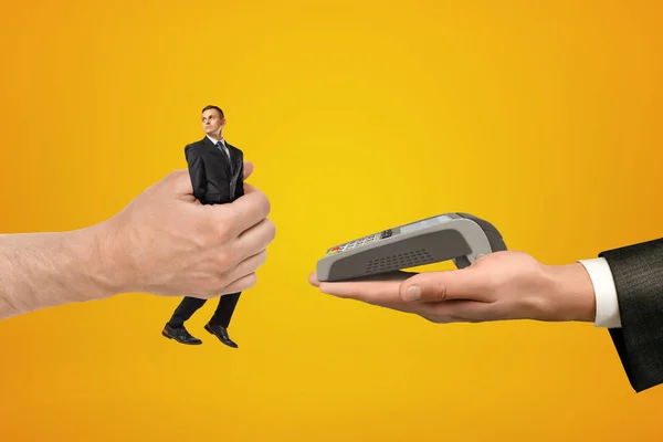Μεγάλο αρσενικό hand περνώντας μικροσκοπικό επιχειρηματία σε ένα άλλο χέρι με PIN pad σε κίτρινο φόντο — Φωτογραφία Αρχείου