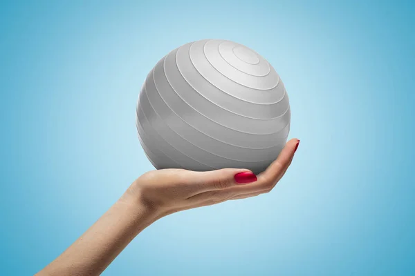 Female hand holding white fitball on blue background — Stock Photo, Image