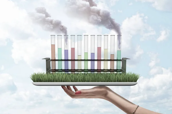 Tubos de ensayo llenos de líquidos de diferentes colores, dos tubos que chorrean humo, de pie en la pantalla cubierta de hierba de la tableta digital en la mano de las mujeres . — Foto de Stock