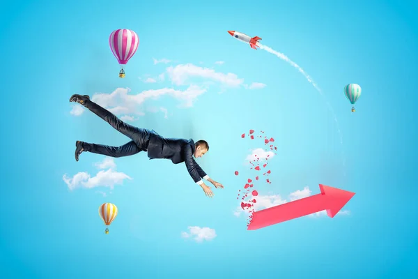 Jonge zakenman in de lucht vallen proberen om rode gebroken grafiek pijl vangen, met hete lucht ballonnen en raket op de achtergrond. — Stockfoto