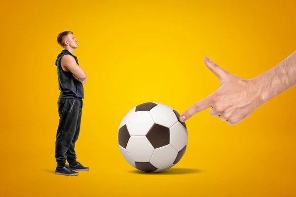 Vista lateral de un pequeño atleta mirando a una gran persona anónima frente a él que está tocando el fútbol entre ellos con solo la pistola de dedo visto al espectador . — Foto de Stock