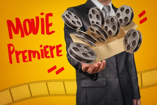 Ανώνυμος επιχειρηματίας αιωρείται κουτί γεμάτο κυλίνδρους ταινία που πετούν έξω από το κουτί σε πορτοκαλί φόντο με τίτλο ταινία Premiere — Φωτογραφία Αρχείου
