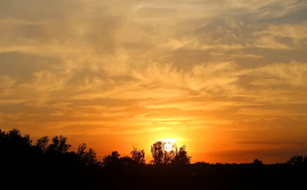 Bela foto de um pôr-do-sol brilhante com nuvens sobre um campo — Fotografia de Stock