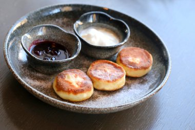 Makro fotoğraf lezzetli parlak peynir kek ile reçel ve ekşi krema bir restoranda karanlık bir plaka üzerinde