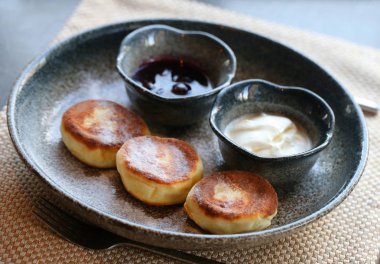 Makro fotoğraf lezzetli parlak peynir kek ile reçel ve ekşi krema bir restoranda karanlık bir plaka üzerinde