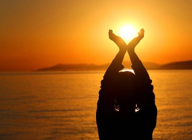 Güneşi tutan güzel bir kızın silüetinin fotoğrafı.