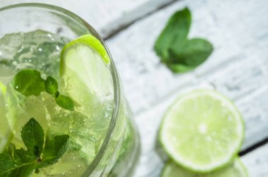 Bir ahşap masada highball cam kireç ve nane yaprakları dilimleri ile Mojito kokteyl. Beyaz arka plan.