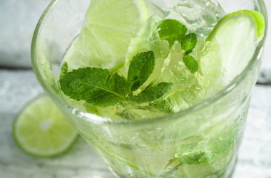 Bir ahşap masada highball cam kireç ve nane yaprakları dilimleri ile Mojito kokteyl. Beyaz arka plan.