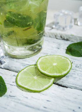 Bir ahşap masada highball cam kireç ve nane yaprakları dilimleri ile Mojito kokteyl. Beyaz arka plan.