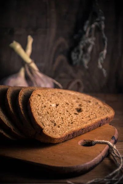 Slices of homemade bread and two heads of garlic on rural background with sackcloth and wood