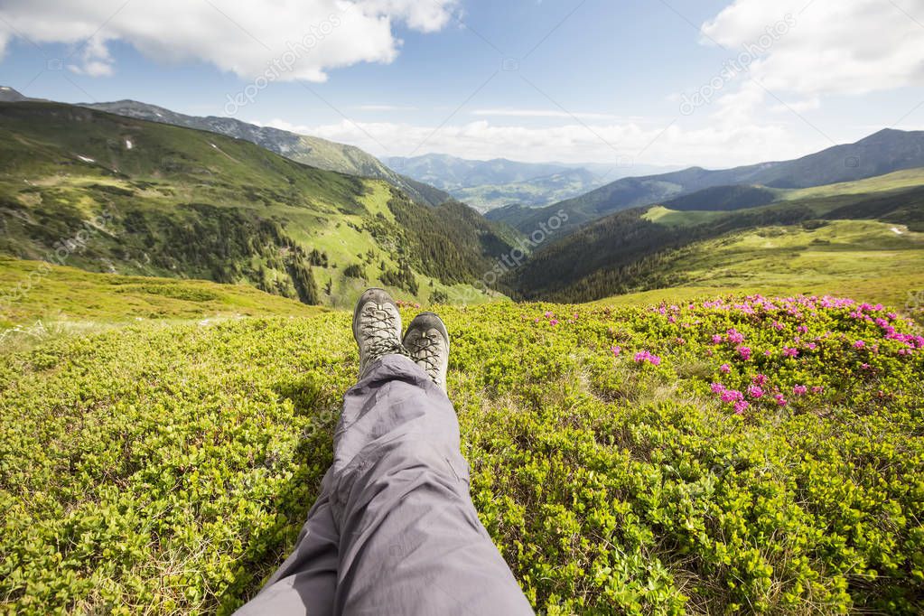 Mountain hiking. Hiker feet resting on top of the hill. Beautiful nature landscape view with Rhododendron flowers