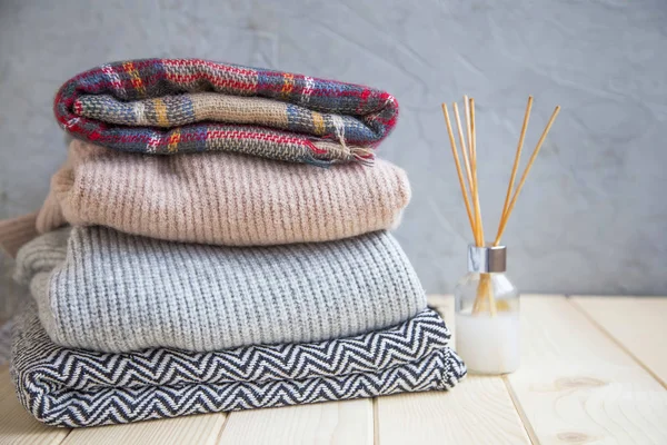 Winter and fall cozy sweaters stack, woolen sweaters and blankets still life with air freshener