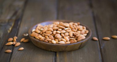 Apricot kernels heap in wooden plate on wooden background, healthy organic apricot kernels