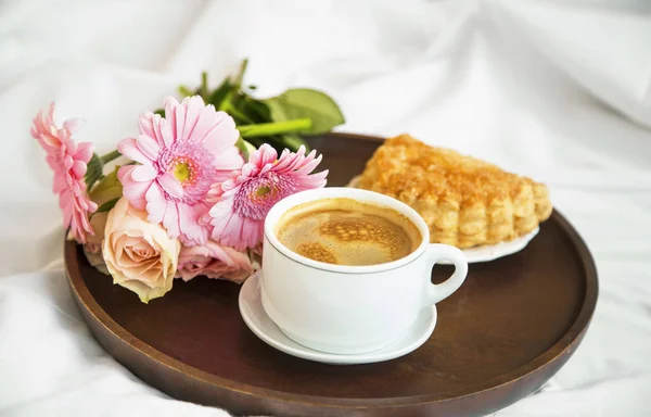 Flowers bouquet with coffee cup and pastry bun on wooden tray in the bed, morning bed breakfast, romantic bed coffee lifestyle